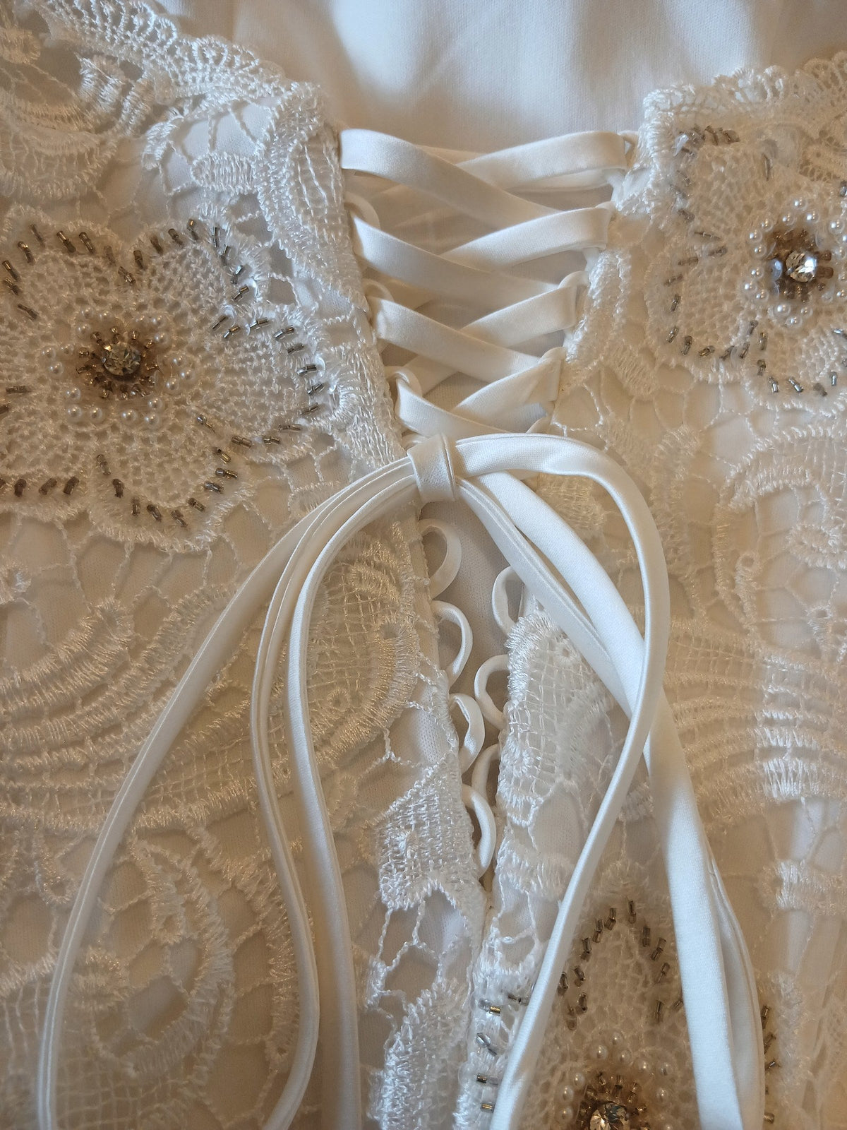 The lace-up back of a corset bodice, satin ribbon threaded through beaded guipure lace